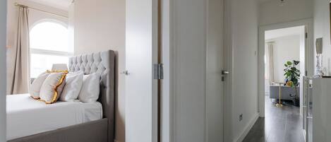 A hotel room with a bed, a wardrobe, a mirror, and a hallway leading to another room.