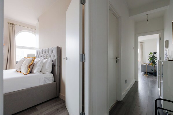Una habitación de hotel con cama, armario, espejo y un pasillo que conduce a otra habitación.