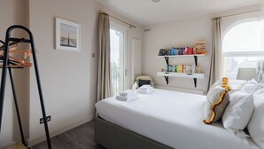 Une chambre d’hôtel avec un lit, une table de chevet, une étagère avec des livres, une fenêtre et un porte-manteau.
