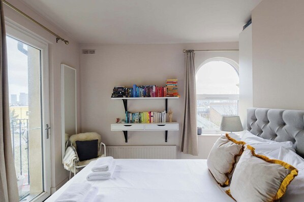 A hotel room with a bed, a bookshelf, a chair, a window, and a view of the city.