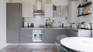 Une cuisine moderne avec des meubles de couleur grise, un four encastré, un évier et un coin repas comprenant une table ronde et des chaises.