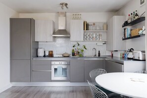 A modern kitchen with grey cabinetry, a built-in oven, a sink, and a dining area with a round table and chairs. - Chic 1BD Flat in Restored English Pub, East London (Greater London)