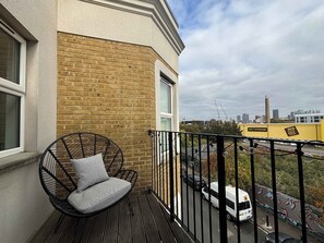 Un balcon avec un fauteuil en osier et une vue sur le paysage urbain.