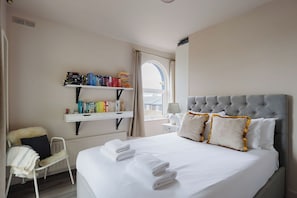 A hotel room with a large bed, a bedside table, a chair, a bookshelf, and a window. - Chic 1BD Flat in Restored English Pub, East London (Greater London)