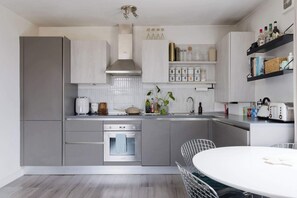 Een moderne keuken met grijze kastjes, een ingebouwde oven, een witte eettafel en een hanglamp.