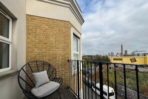 Un balcon avec un fauteuil en osier et une vue sur le paysage urbain.