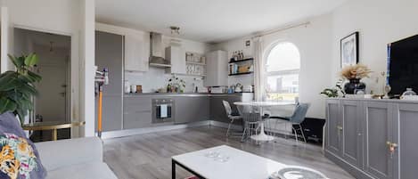 A modern kitchen with grey cabinets, a dining area with a white table and chairs, and a living room with a sofa and a coffee table.