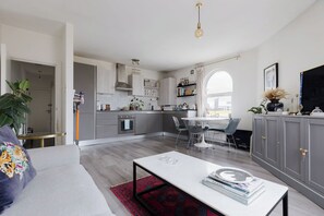 A modern kitchen with grey cabinets, a dining area with a white table and chairs, and a living room with a sofa and a coffee table. - Chic 1BD Flat in Restored English Pub, East London (Greater London)