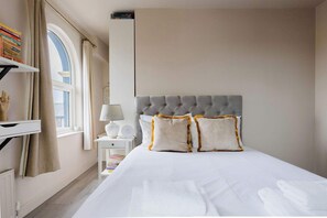 Een netjes ingerichte hotelkamer met een groot bed, een nachtkastje met een lamp, een raam met gordijnen en een boekenkast met boeken.