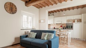 A living room with a blue sofa, a wooden ceiling, a kitchen with white cabinets, and a tiled floor. - At Chica's House - Lucca with Private Parking and Outdoor Space (Lucca)