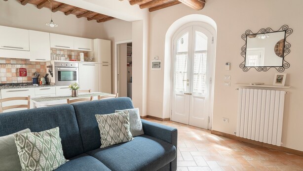 A living room with a sofa, a kitchen with cabinets and appliances, and a white radiator. - At Chica's House - Lucca with Private Parking and Outdoor Space (Lucca)