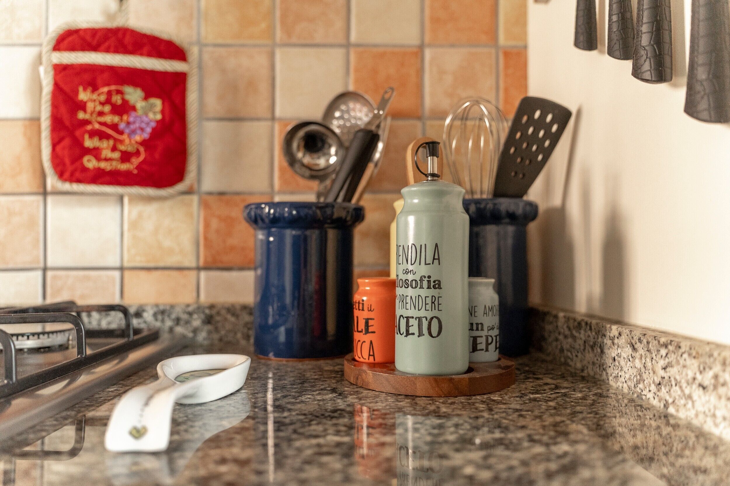 A kitchen counter with a gas stove, a white electric kettle, and various kitchen utensils in holders.