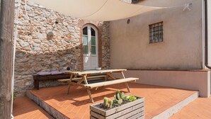 A patio with a wooden table and benches, a stone wall, a window, and a planter with cacti. - At Chica's House - Lucca with Private Parking and Outdoor Space (Lucca)