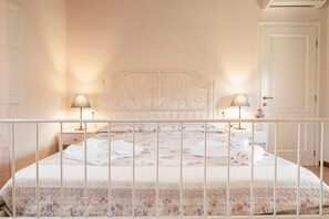 Una cama con colcha estampada, dos lámparas de noche y un cabecero blanco.