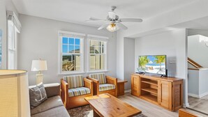A living room with a sofa, two armchairs, a coffee table, a TV, and a ceiling fan.