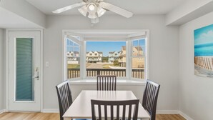 A dining area with a table and chairs, a ceiling fan, and a view of a residential neighborhood through large windows.