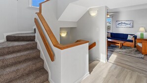 Una escalera con barandillas de madera que conduce a una sala de estar con un sofá azul, un cuadro y una lámpara.