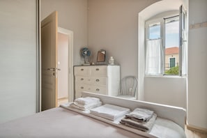 Un dormitorio con cama, cómoda, espejo y ventana con vista a un edificio.