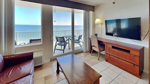 Una camera d'albergo con un balcone, una TV, un armadietto in legno e un divano in pelle.
