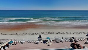 A beach view with a pier, lounge chairs, and umbrellas.