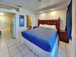 Une chambre à coucher avec un grand lit, une tête de lit en bois, une table de chevet et une salle de bain visible à travers une porte ouverte.