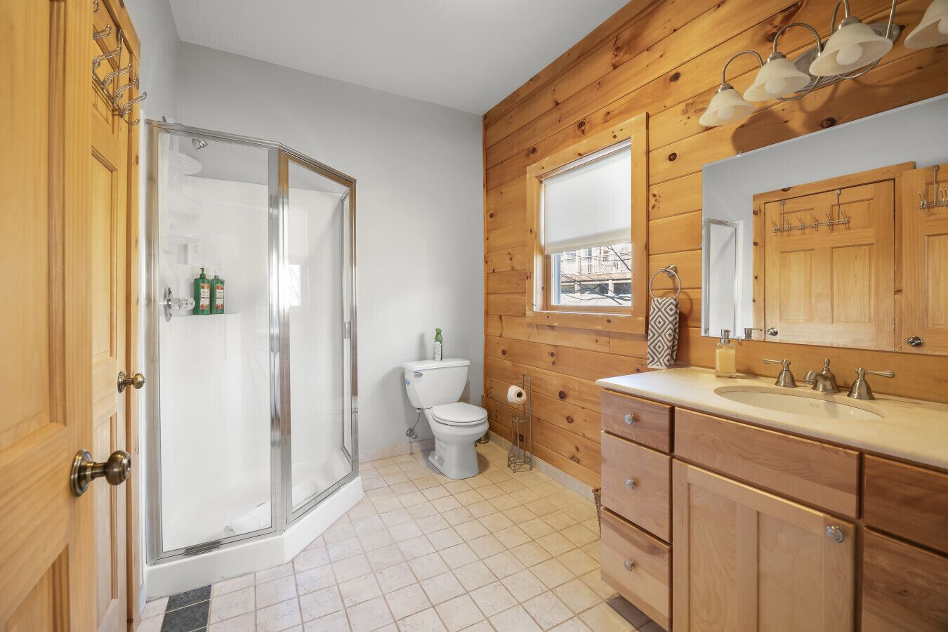 Ein Badezimmer mit Holzwänden, einer Glasdusche, einer Toilette und einem Waschtisch mit Spiegel.