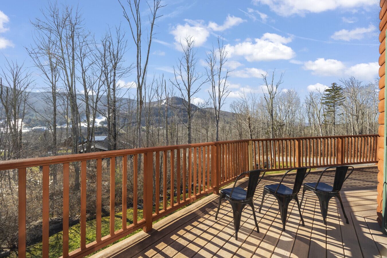 A wooden deck with a railing, two chairs, and a view of a mountainous landscape.