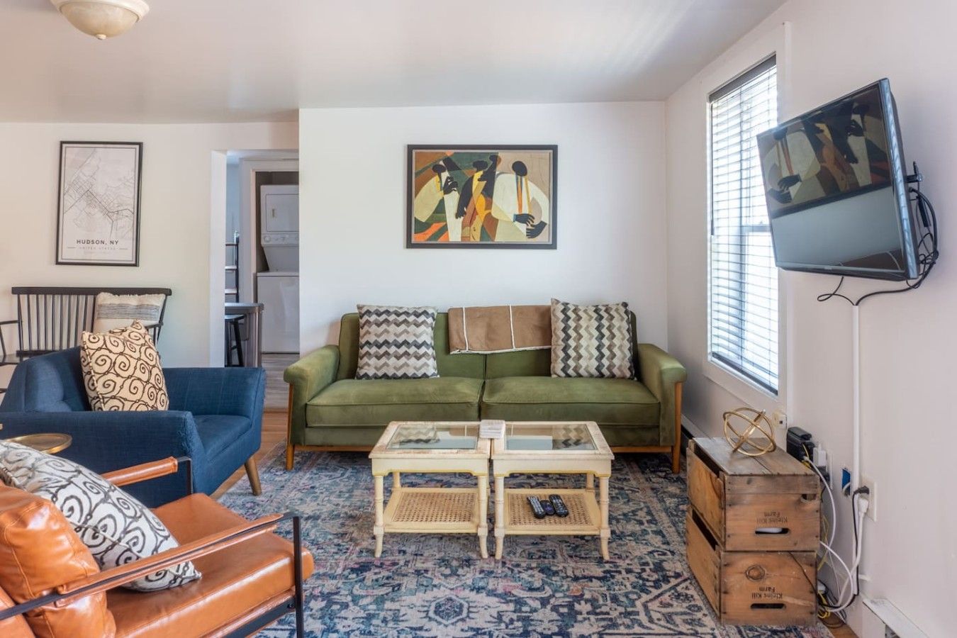 A living room with a green sofa, a blue armchair, a coffee table, and a television mounted on the wall.