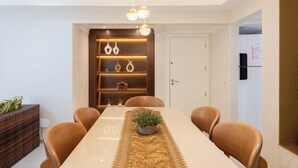 Un comedor con una mesa larga, seis sillas, una araña y una unidad de pared decorativa con estantes.