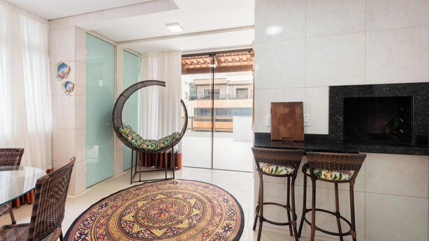 Una sala de estar moderna con una mesa de comedor de vidrio, sillas de mimbre, un sofá curvo, una alfombra estampada, un televisor y una chimenea.