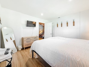 A bedroom with a large bed, a wardrobe, a television on the wall, and a door leading to another room.