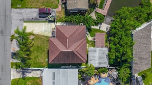 An aerial view of a residential area with a prominent house featuring a red roof, a swimming pool, and lush greenery.