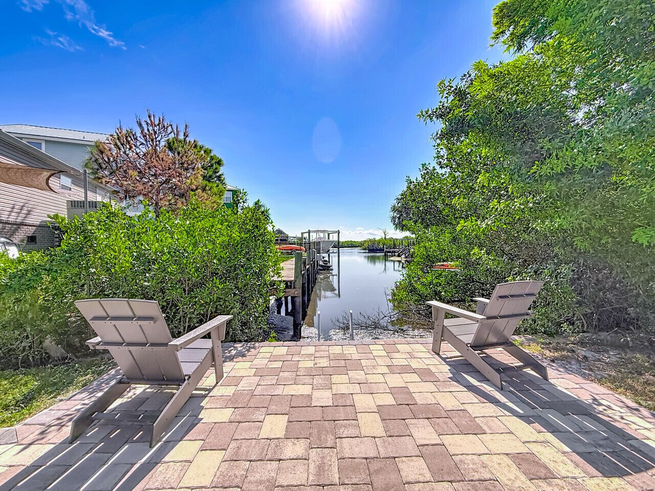 A waterfront patio with two Adirondack chairs, a dock, and a clear view of the water.