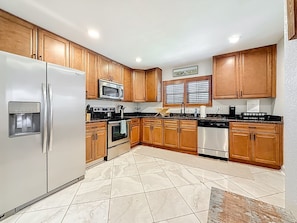 A kitchen with wooden cabinets, stainless steel appliances, and a tiled floor.
