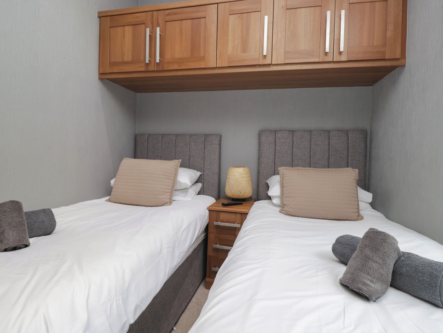 Una habitació d'hotel amb dos llits, armaris de fusta a la part superior i una taula de nit amb una làmpada.