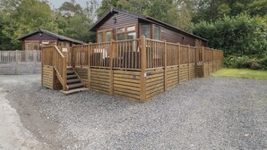 Eine Holzhütte mit einer Terrasse und Treppe, umgeben von Kies und Bäumen.