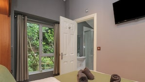Ein Hotelzimmer mit Bett, einem Fenster mit Vorhängen, einem durchgegangenen Türspalt erkennbaren Badezimmer und einem an der Wand befestigten Flachbildfernseher.