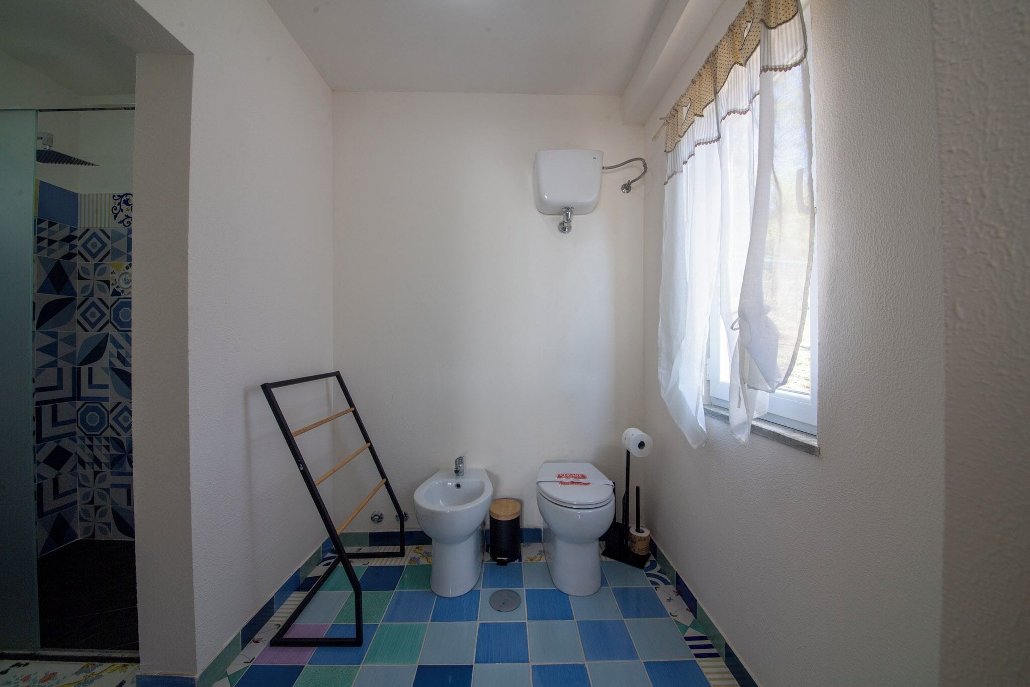A small bathroom with a toilet, bidet, and a window with curtains.