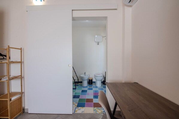 A small, narrow bathroom with a white door, a wooden shelf, and a colorful checkered floor. - Casa Mario immersed in the Lazio countryside (Rome)