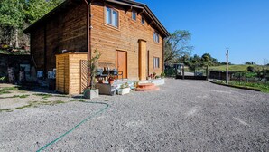 A wooden cabin with a gravel driveway, a small porch with outdoor seating, and a fenced yard. - Casale in legno nella natura laziale (Rome)