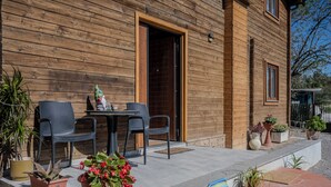 A wooden building with a patio area featuring two chairs, a table, and potted plants. - Casale in legno nella natura laziale (Rome)