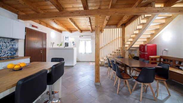A modern kitchen with wooden beams, a dining area with a long table and chairs, and a staircase leading to an upper level. - Casale in legno nella natura laziale (Rome)