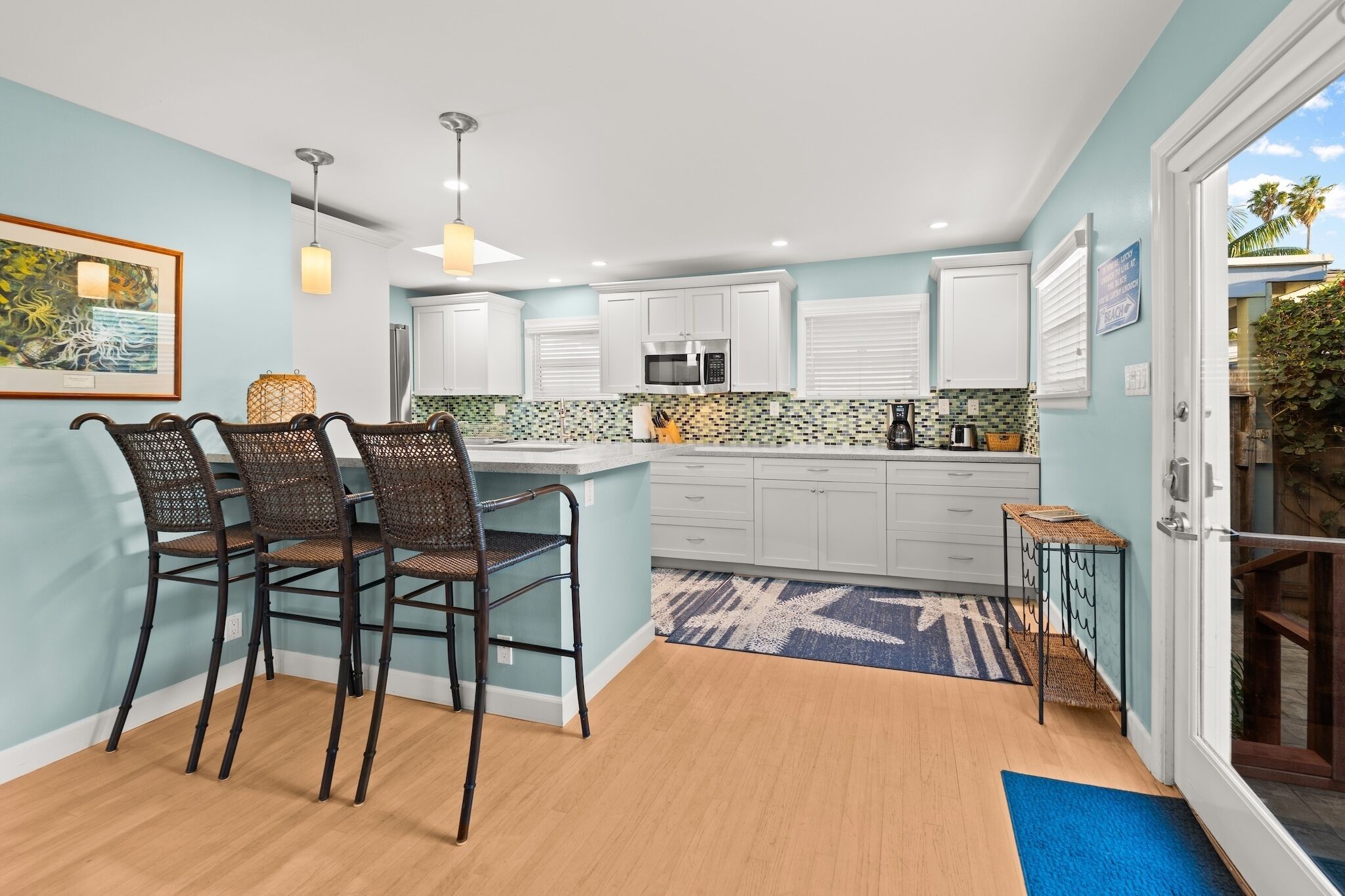 A modern kitchen with white cabinets, a microwave, and a coffee maker. There are three wicker chairs at a dining table.