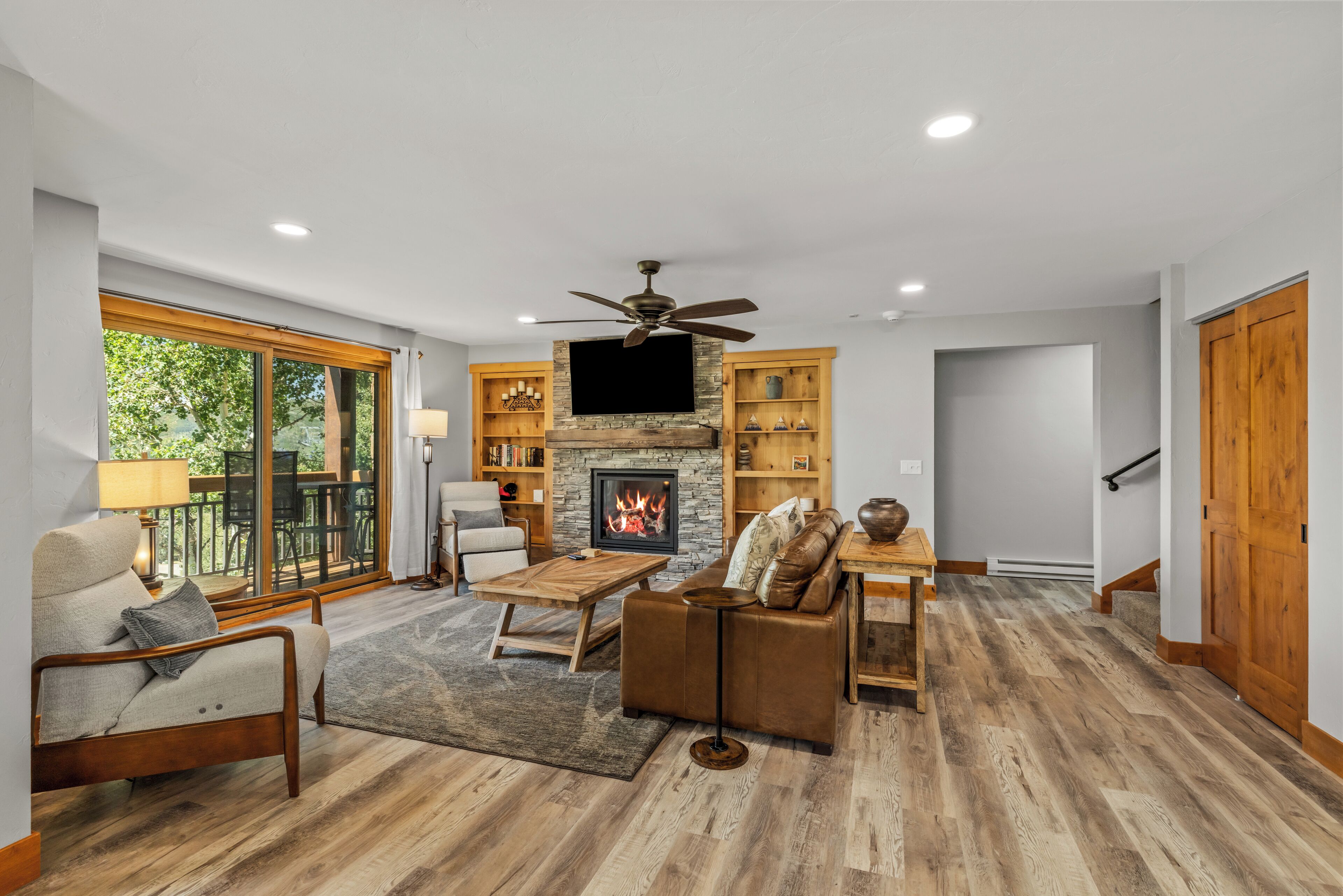 A spacious living room with a fireplace, comfortable seating, and a large window overlooking greenery.