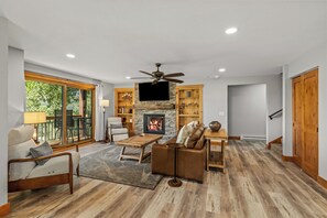 A spacious living room with a fireplace, comfortable seating, and a large window overlooking greenery.