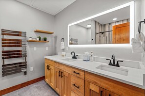 A modern bathroom with two sinks, a large mirror, wooden cabinets, and a towel rack.