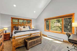 A bedroom with a wooden bed, a desk, and a large window.
