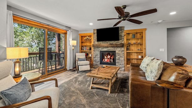 A spacious living room with a fireplace, comfortable seating, and a television mounted on the wall. - Norwegian Log condo - Sleeps 8! (Steamboat Springs)