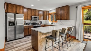 A modern kitchen with wooden cabinets, stainless steel appliances, and a large island with bar stools. - Norwegian Log condo - Sleeps 8! (Steamboat Springs)