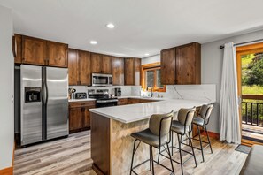 A modern kitchen with wooden cabinets, stainless steel appliances, and a large island with bar stools.